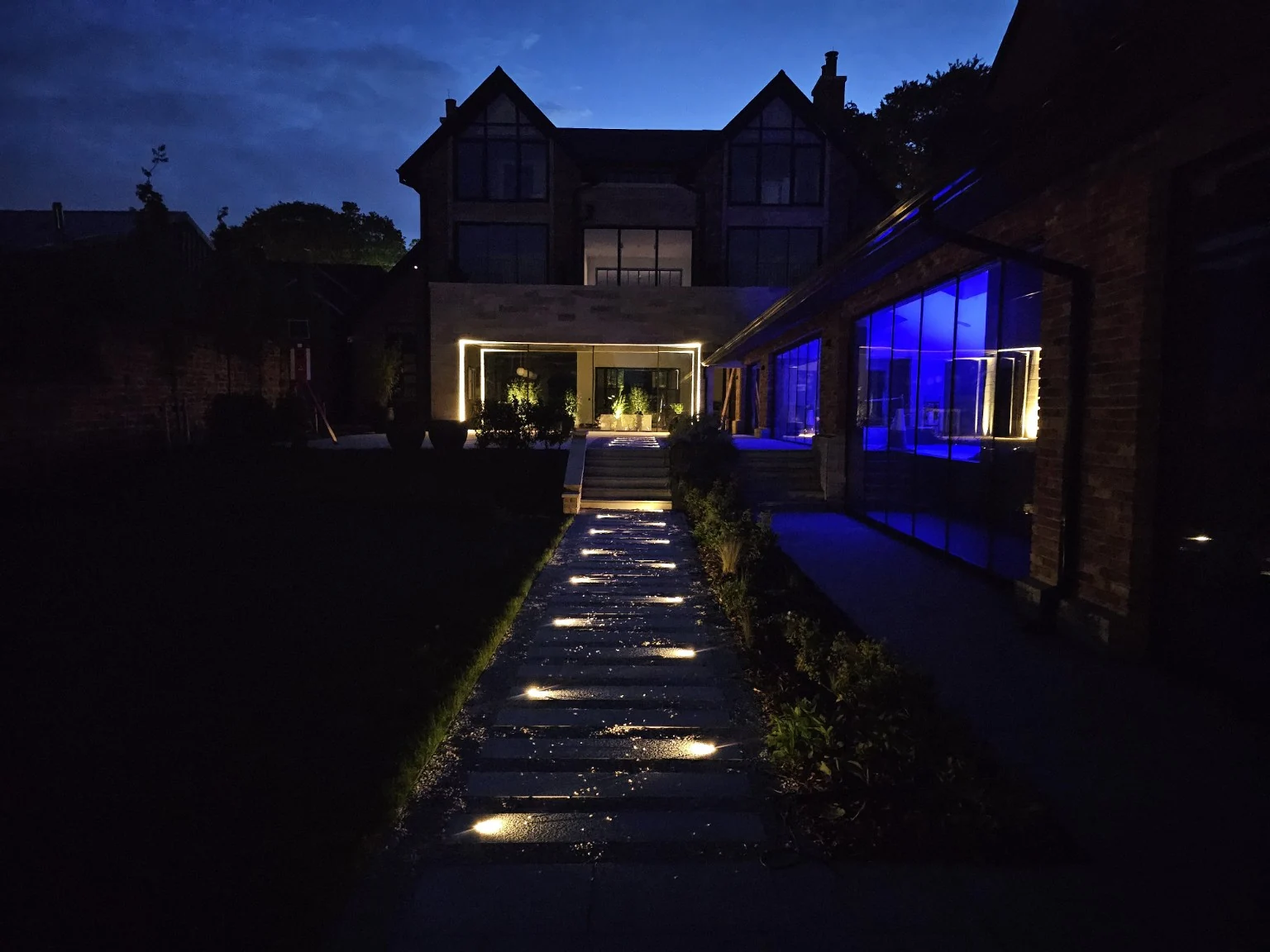 Lit pathways, steps and building elevation at dusk