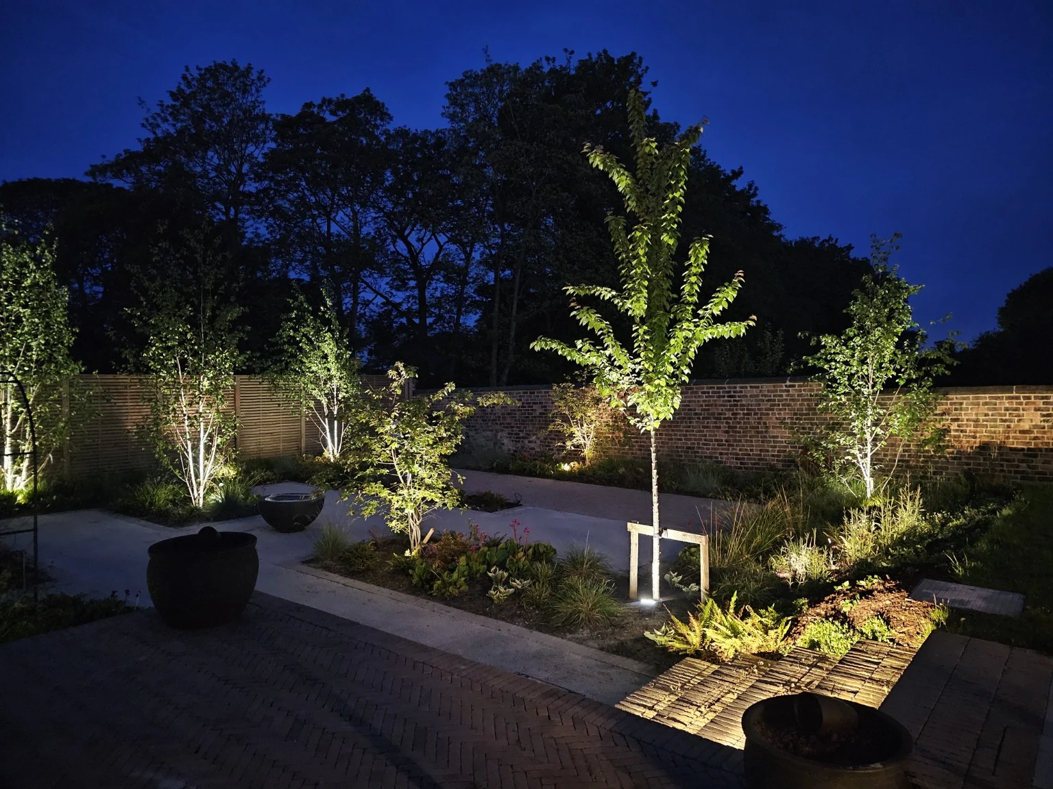 Layered lighting across mature trees, planting and paths at dusk